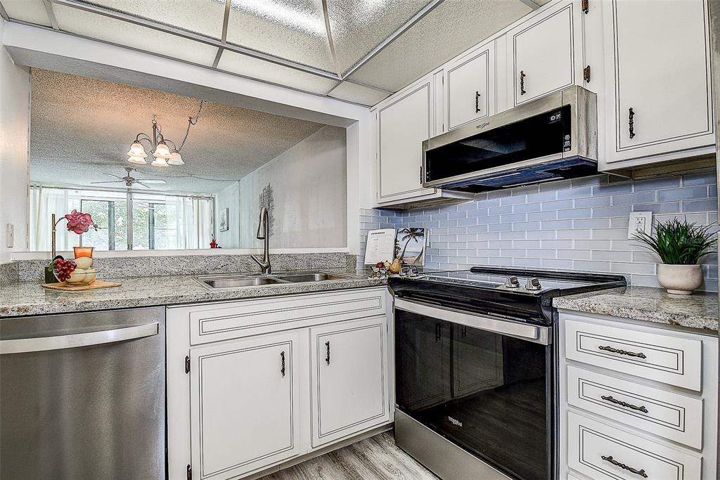 A kitchen with white cabinets, granite countertops, stainless steel appliances, and a pass-through window — 12300 VONN ROAD UNIT 7203, LARGO, FL