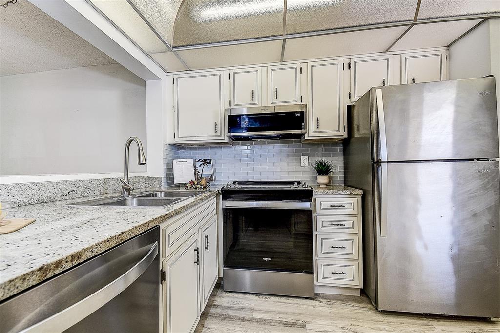 A kitchen features white cabinets, stainless steel appliances, granite countertops, and a gray subway tile backsplash — 12300 VONN ROAD UNIT 7203, LARGO, FL
