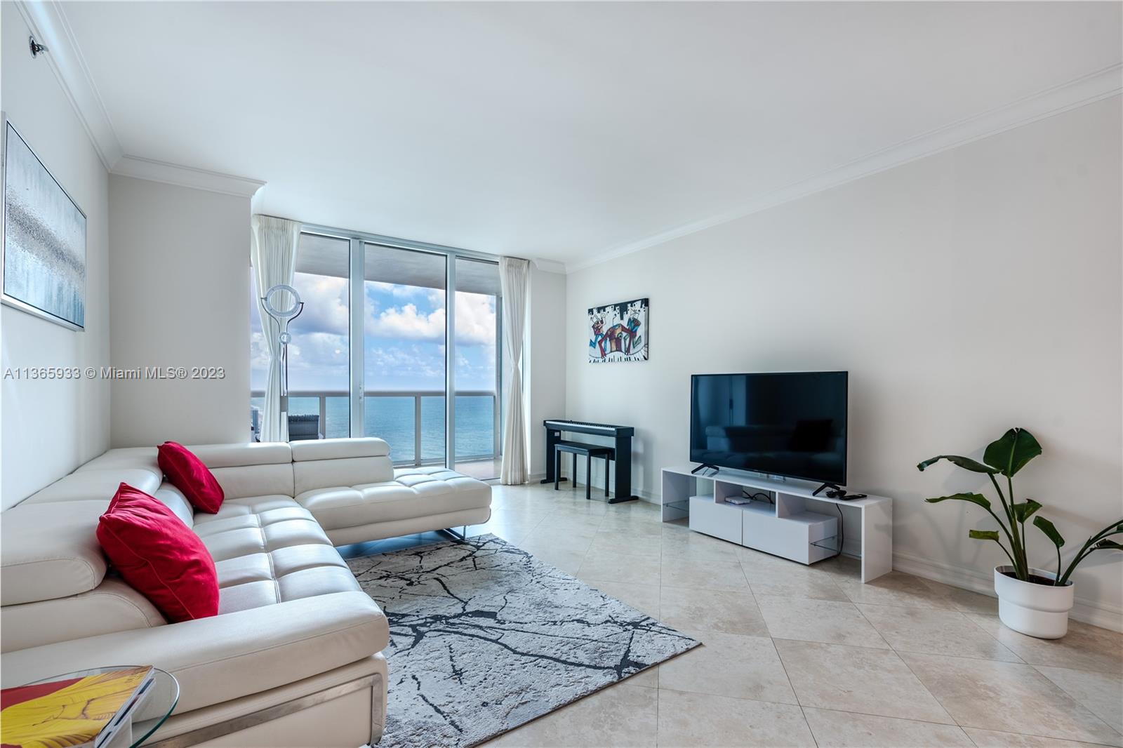 A living room features a white sectional sofa, a television, and a balcony overlooking the ocean — 1830 S Ocean Dr Available # 3511, Hallandale Beach FL 33009, HALLANDALE BEACH, FL