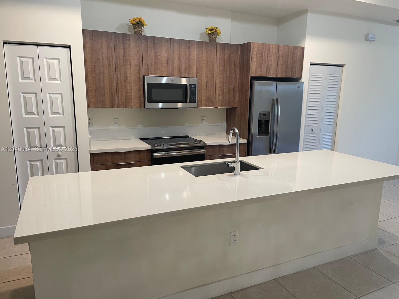 A modern kitchen features wood-tone cabinets, stainless steel appliances, and a large white island — 8025 NW 104th Ave # 31, Doral FL 33178, DORAL, FL