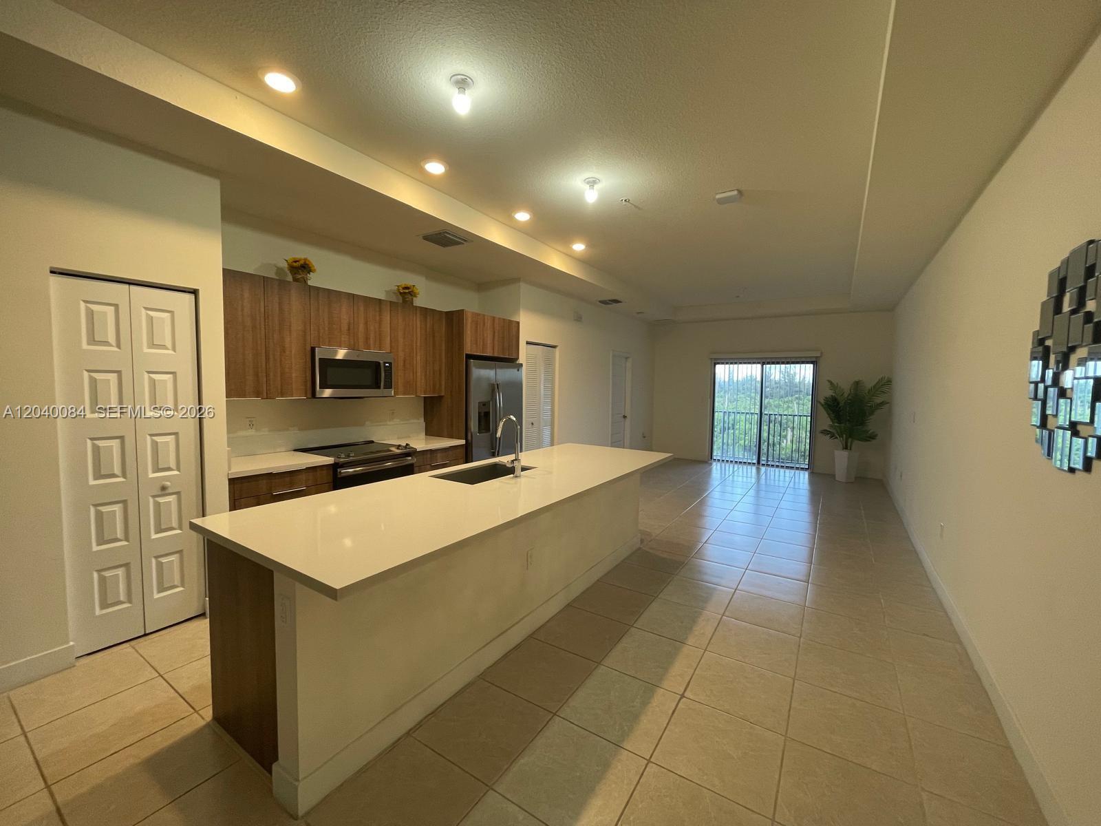 A modern kitchen features a long white island, wood-toned cabinetry, and tile flooring — 8025 NW 104th Ave # 31, Doral FL 33178, DORAL, FL