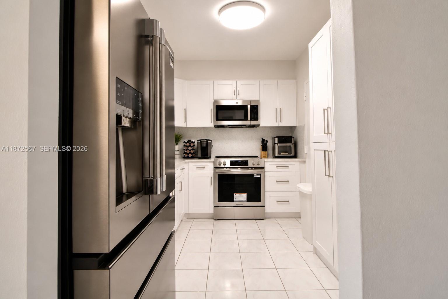 A kitchen features white cabinetry, stainless steel appliances, and white floor tiles — 1950 S Ocean Dr # 11D, Hallandale Beach FL 33009, HALLANDALE BEACH, FL