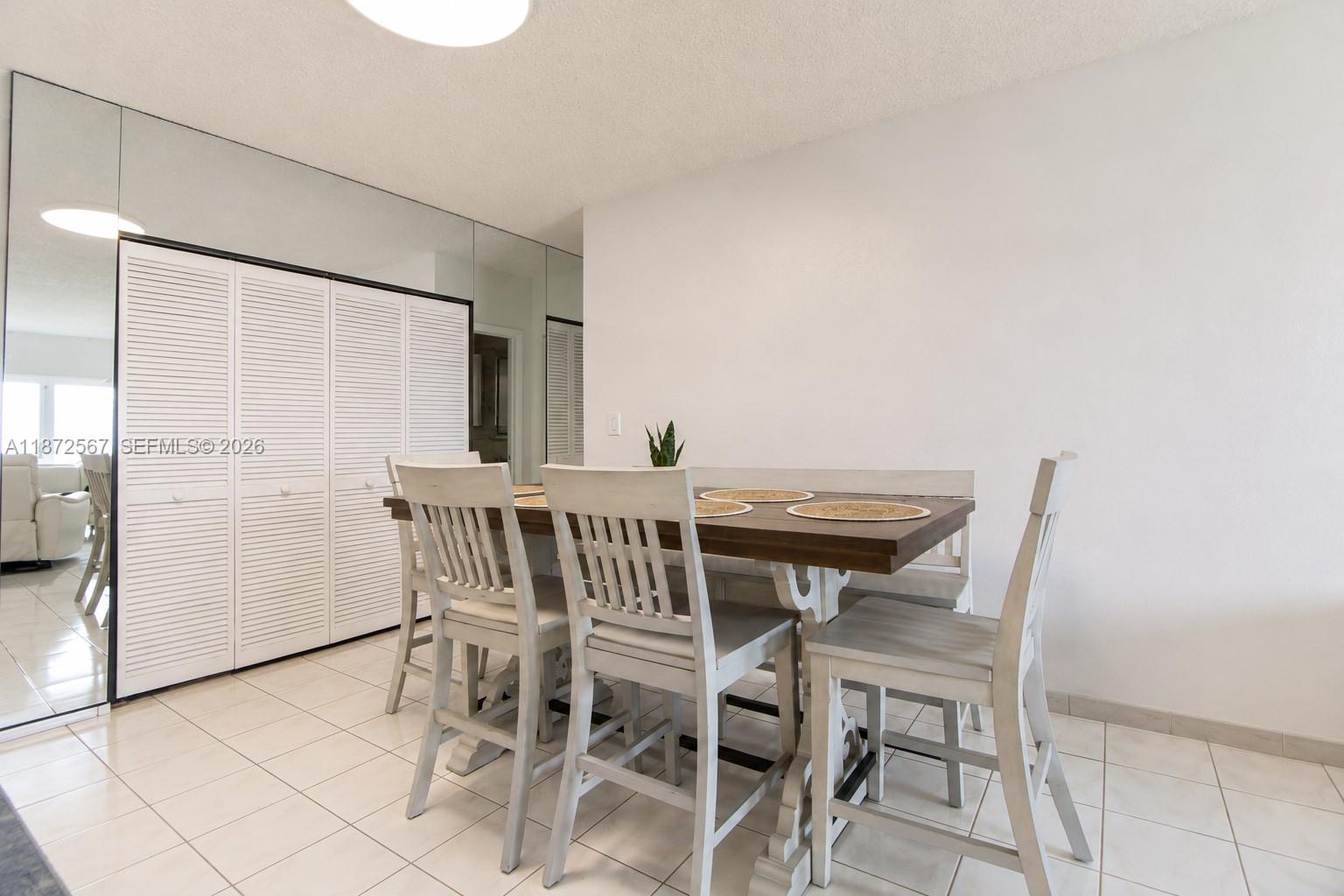 A dining area features a wooden table with white chairs, tiled floors, and mirrored closet doors — 1950 S Ocean Dr # 11D, Hallandale Beach FL 33009, HALLANDALE BEACH, FL