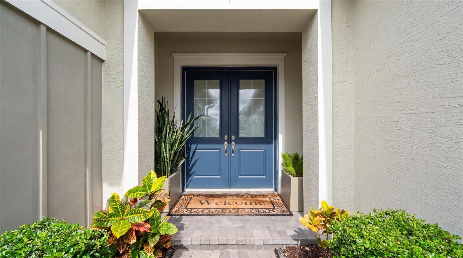 A blue double front door with glass panels is framed by light-colored walls and greenery — 5919 Jasmine Lane, Westlake FL 33470, WESTLAKE, FL