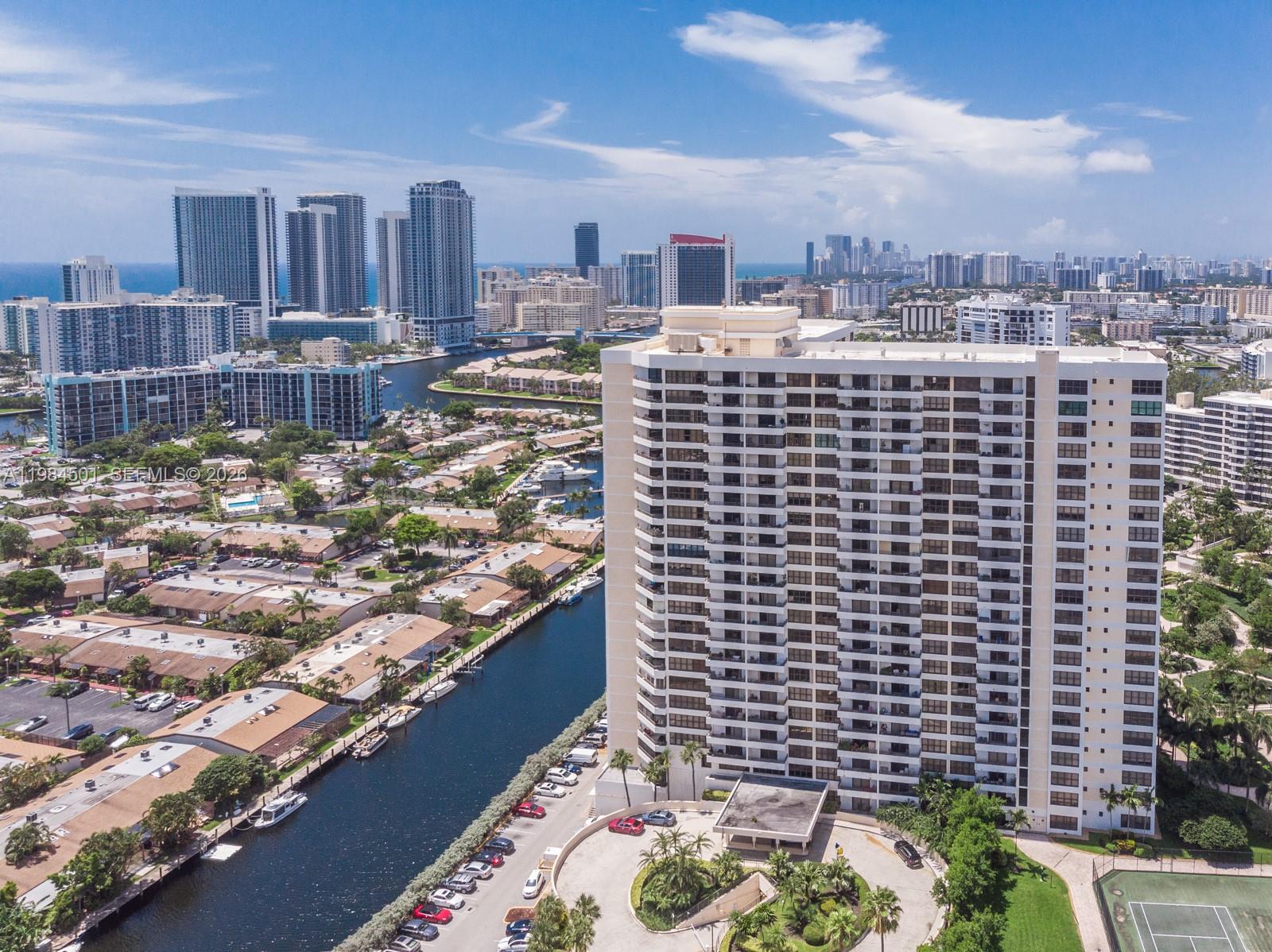 An aerial view shows a tall residential building next to a canal and city skyline — 2500 Parkview Dr # 509, Hallandale Beach FL 33009, HALLANDALE BEACH, FL