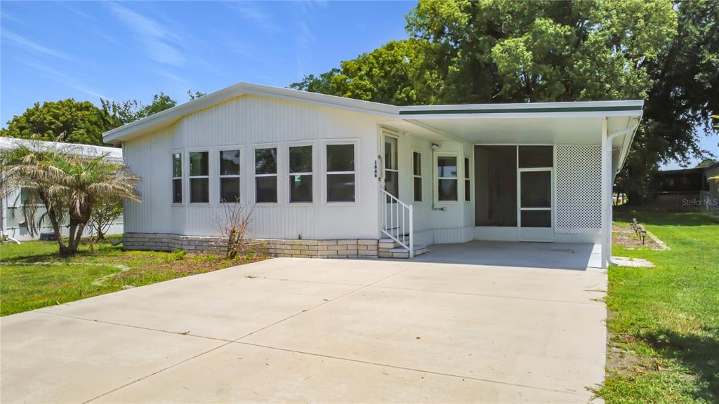A white manufactured home features a concrete driveway, a carport, and a screened-in porch area — 1666 ELKHART CIRCLE, TAVARES, FL