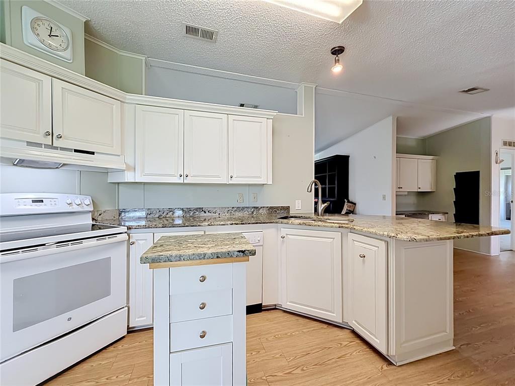 A kitchen features white cabinets, granite countertops, a small island, and light wood flooring — 1666 ELKHART CIRCLE, TAVARES, FL