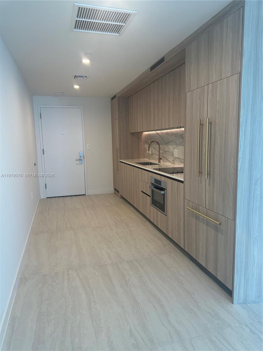 A modern kitchen features wood-grain cabinetry, marble backsplash, and stainless steel appliances — 77 SE 5th # 2514, Miami FL 33131, MIAMI, FL