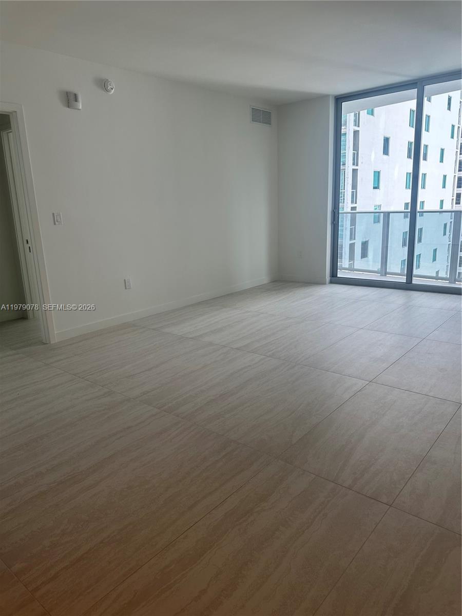 An empty room features light-colored tile flooring, white walls, and a large glass balcony door — 77 SE 5th # 2514, Miami FL 33131, MIAMI, FL