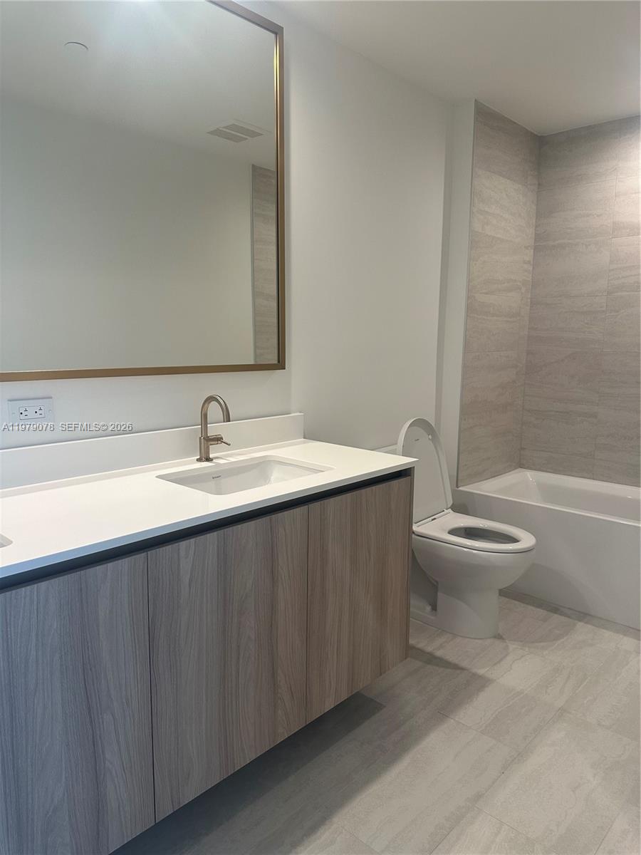 A modern bathroom features a wood-grain vanity, white countertop, rectangular mirror, and a tiled bathtub — 77 SE 5th # 2514, Miami FL 33131, MIAMI, FL