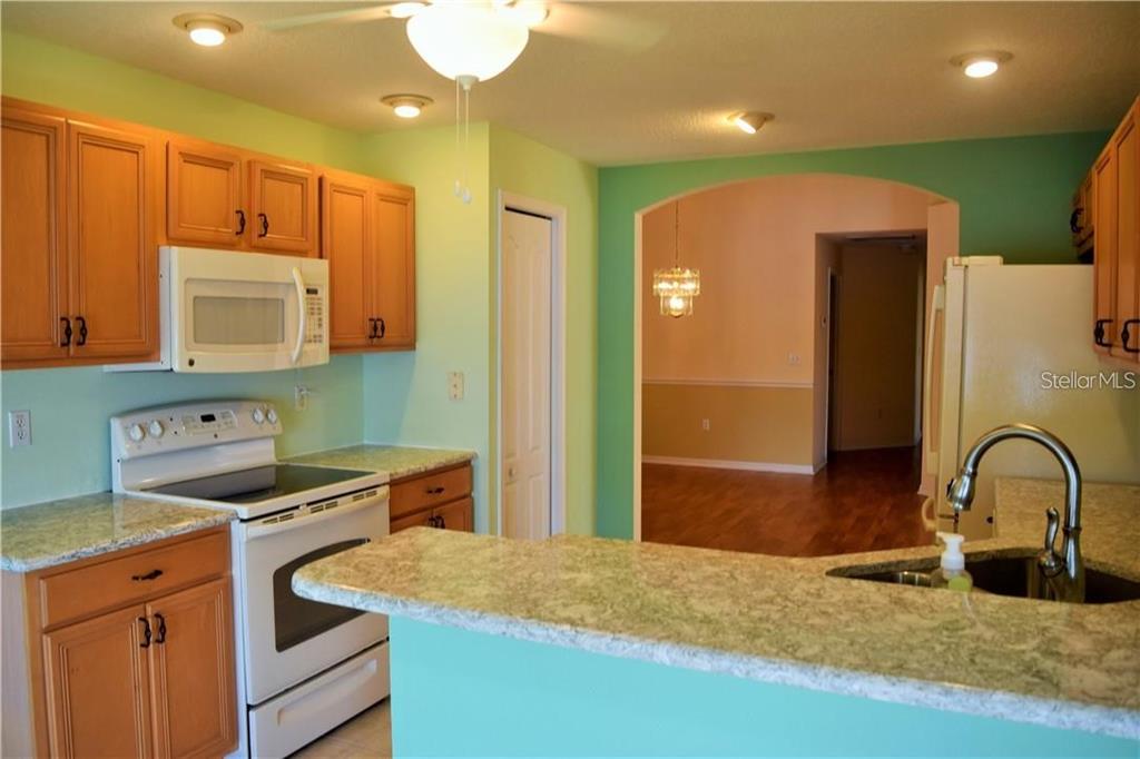 A kitchen features light green walls, wooden cabinets, a white stove, and a granite countertop — 29530 WAGGLE DRIVE, SAN ANTONIO, FL