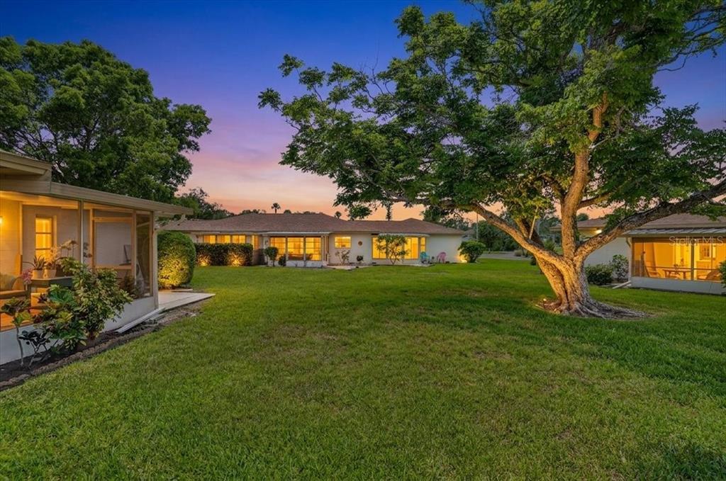 A grassy backyard features a large tree, a screened-in porch, and a single-story house — 2719 51ST AVENUE W, BRADENTON, FL
