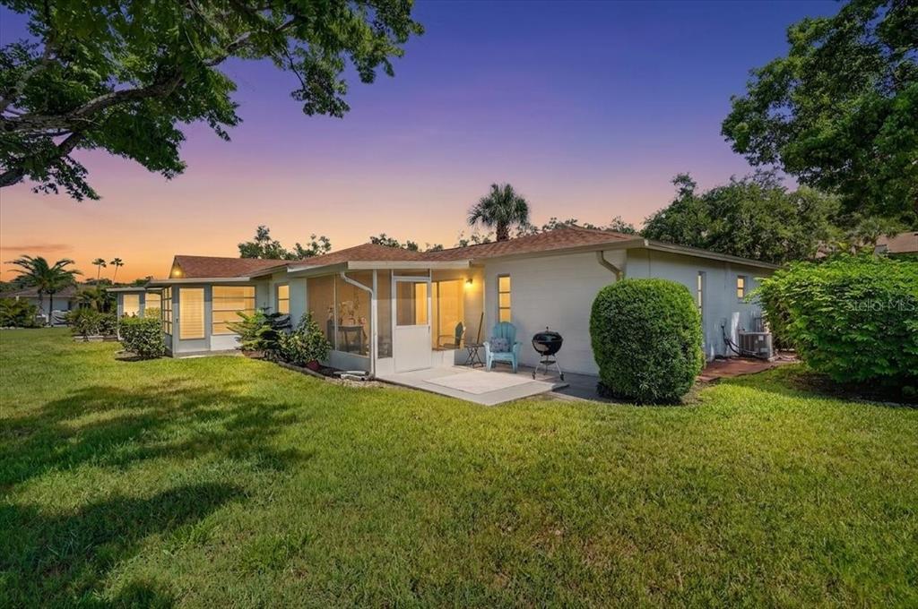 A backyard view of a single-story house with a screened-in porch and a grassy lawn — 2719 51ST AVENUE W, BRADENTON, FL