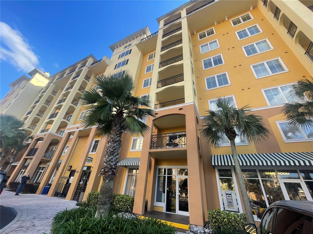 A low-angle exterior view of a multi-story yellow building with balconies and palm trees — 8112 POINCIANA BOULEVARD UNIT 1509, ORLANDO, FL