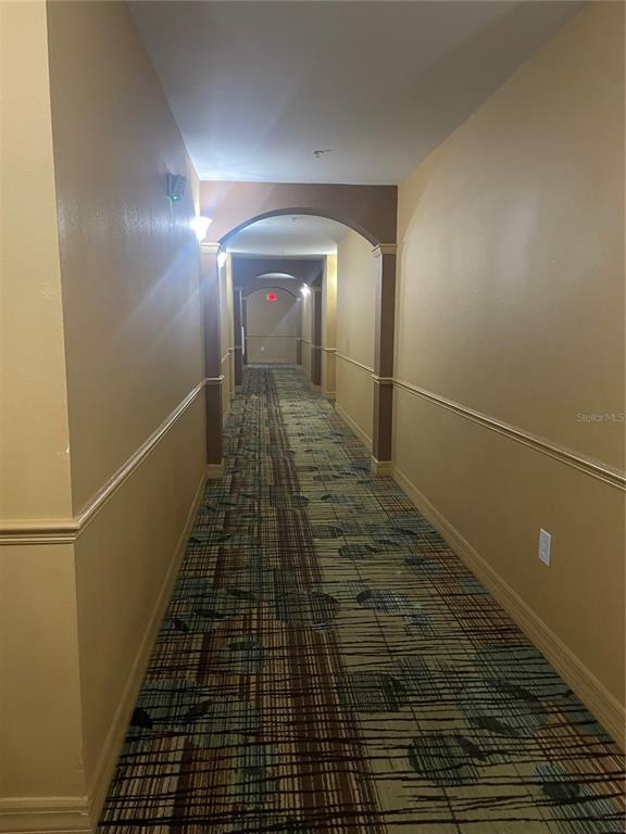 A long indoor hallway features tan walls, a patterned carpet, and multiple arched architectural transitions — 8112 POINCIANA BOULEVARD UNIT 1509, ORLANDO, FL