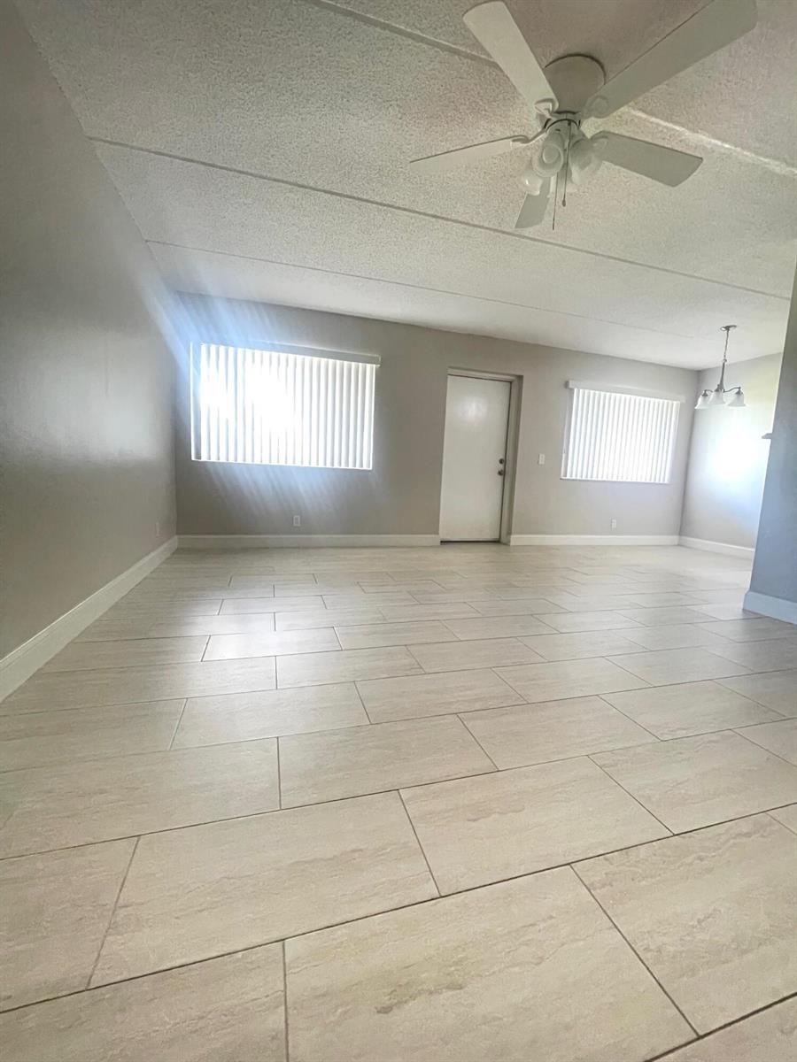 An empty room features light-colored tile flooring, gray walls, a ceiling fan, and two windows — 100 Village Green Circle E # 112, Palm Springs FL 33461, PALM SPRINGS, FL
