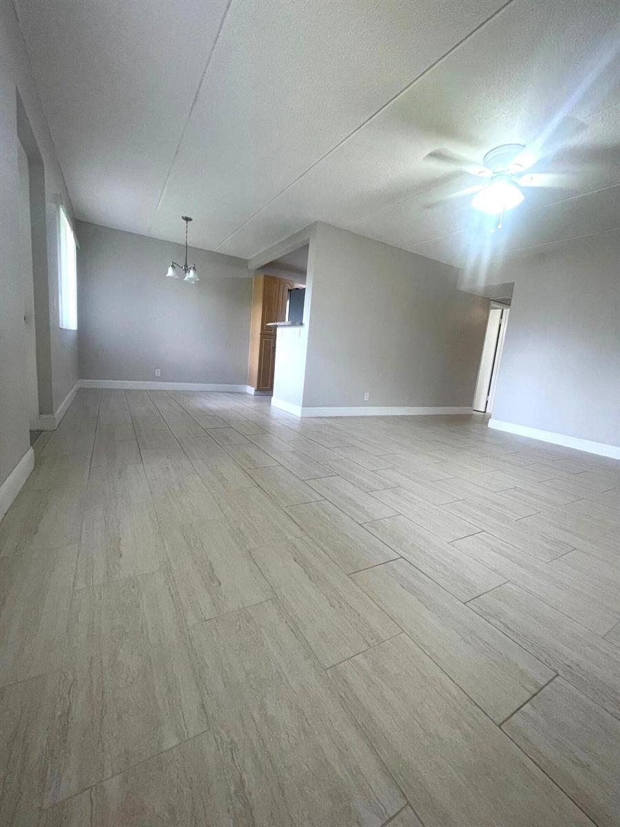 An open-concept living area features light-colored wood-look tile flooring and neutral gray walls — 100 Village Green Circle E # 112, Palm Springs FL 33461, PALM SPRINGS, FL