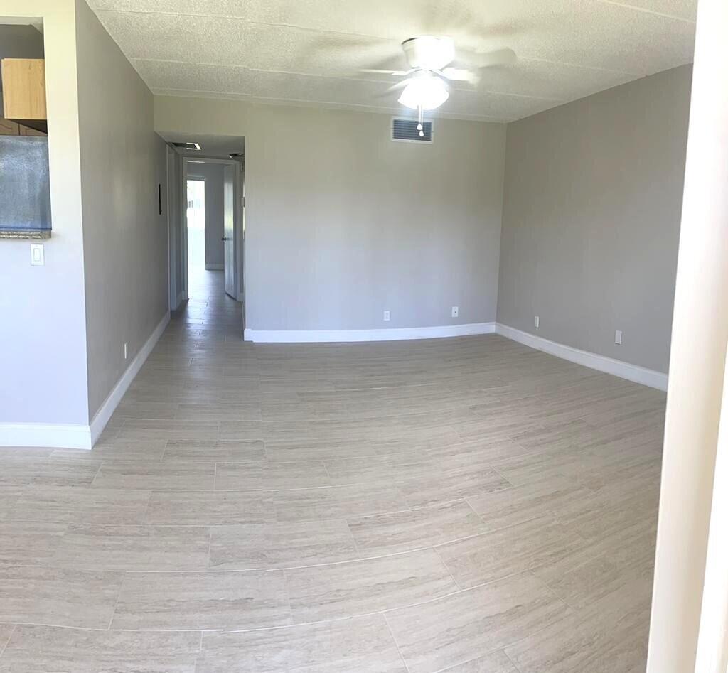 An empty living room features light gray walls, wood-look tile flooring, and a ceiling fan — 100 Village Green Circle E # 112, Palm Springs FL 33461, PALM SPRINGS, FL