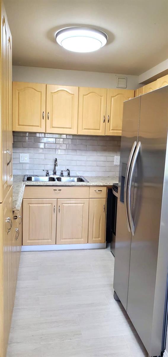A kitchen features light wood cabinets, stainless steel appliances, and a gray subway tile backsplash — 100 Village Green Circle E # 112, Palm Springs FL 33461, PALM SPRINGS, FL
