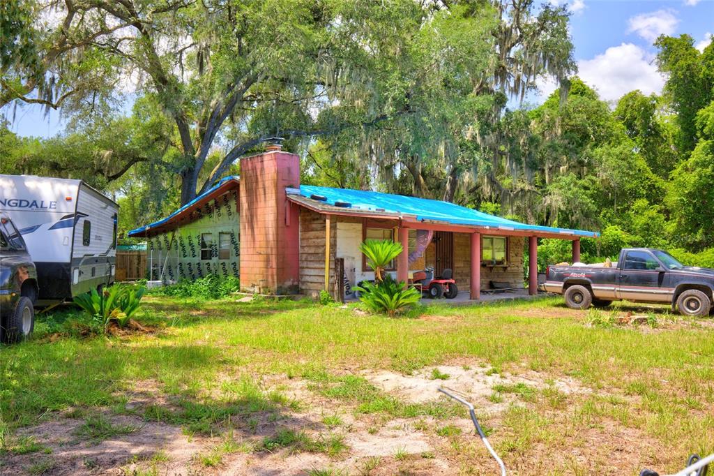 A single-story house with a blue tarp roof and exposed construction wrap under large trees — 18938 SE 105TH LANE, OCKLAWAHA, FL