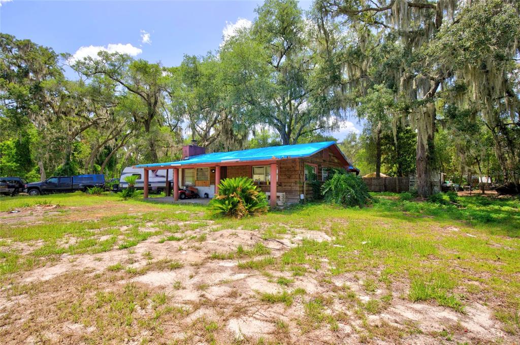 A single-story log cabin with a bright blue metal roof sits on a grassy lot — 18938 SE 105TH LANE, OCKLAWAHA, FL