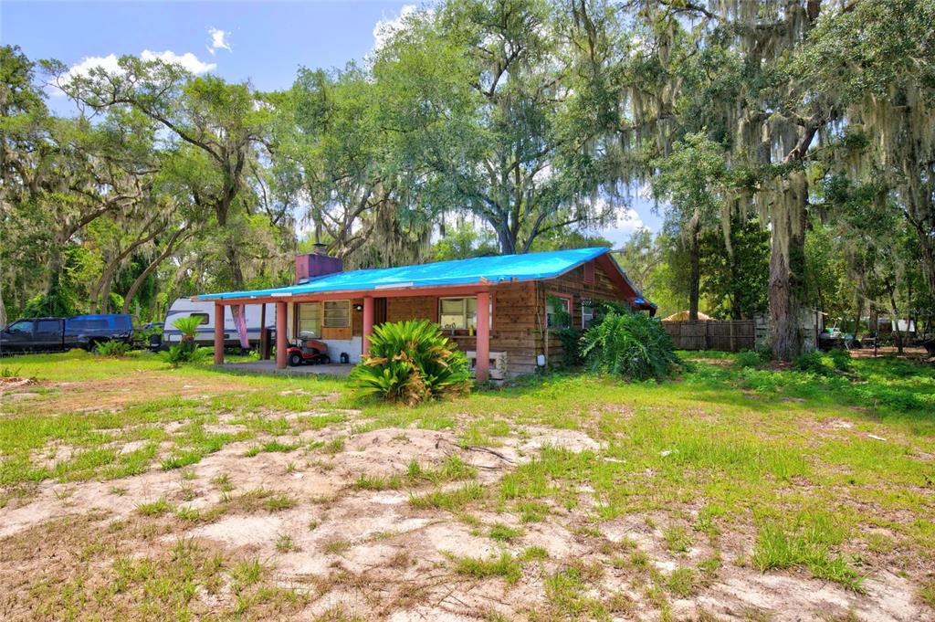 A single-story house with a blue tarp roof sits on a grassy, wooded lot — 18938 SE 105TH LANE, OCKLAWAHA, FL