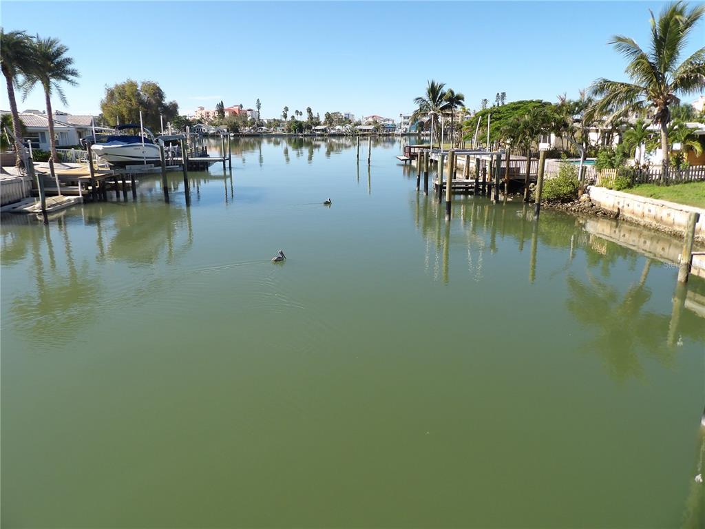 A view of a calm canal lined with boat docks, palm trees, and residential homes — 497 NORMANDY ROAD, MADEIRA BEACH, FL