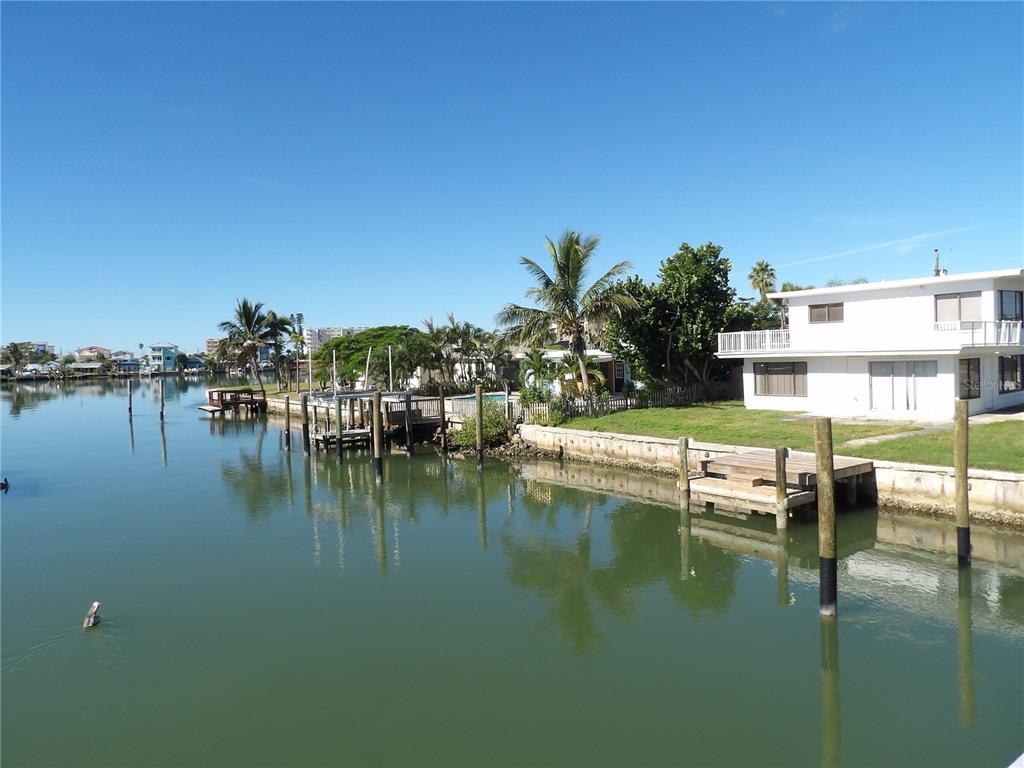 A waterfront view of a white house with a dock and palm trees — 497 NORMANDY ROAD, MADEIRA BEACH, FL