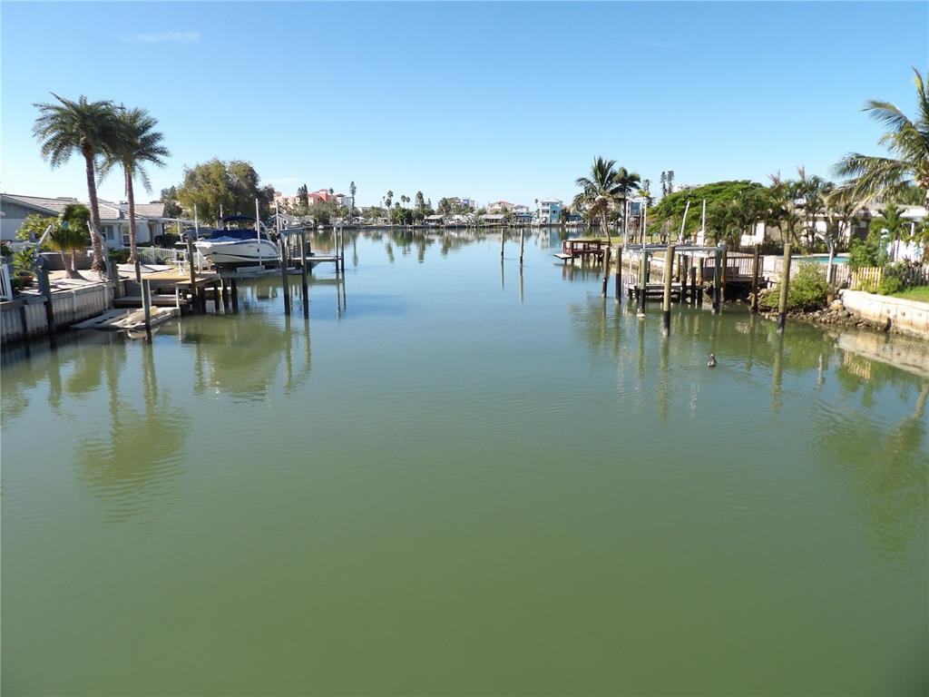 A view of a calm canal lined with boat docks, palm trees, and residential homes — 497 NORMANDY ROAD, MADEIRA BEACH, FL