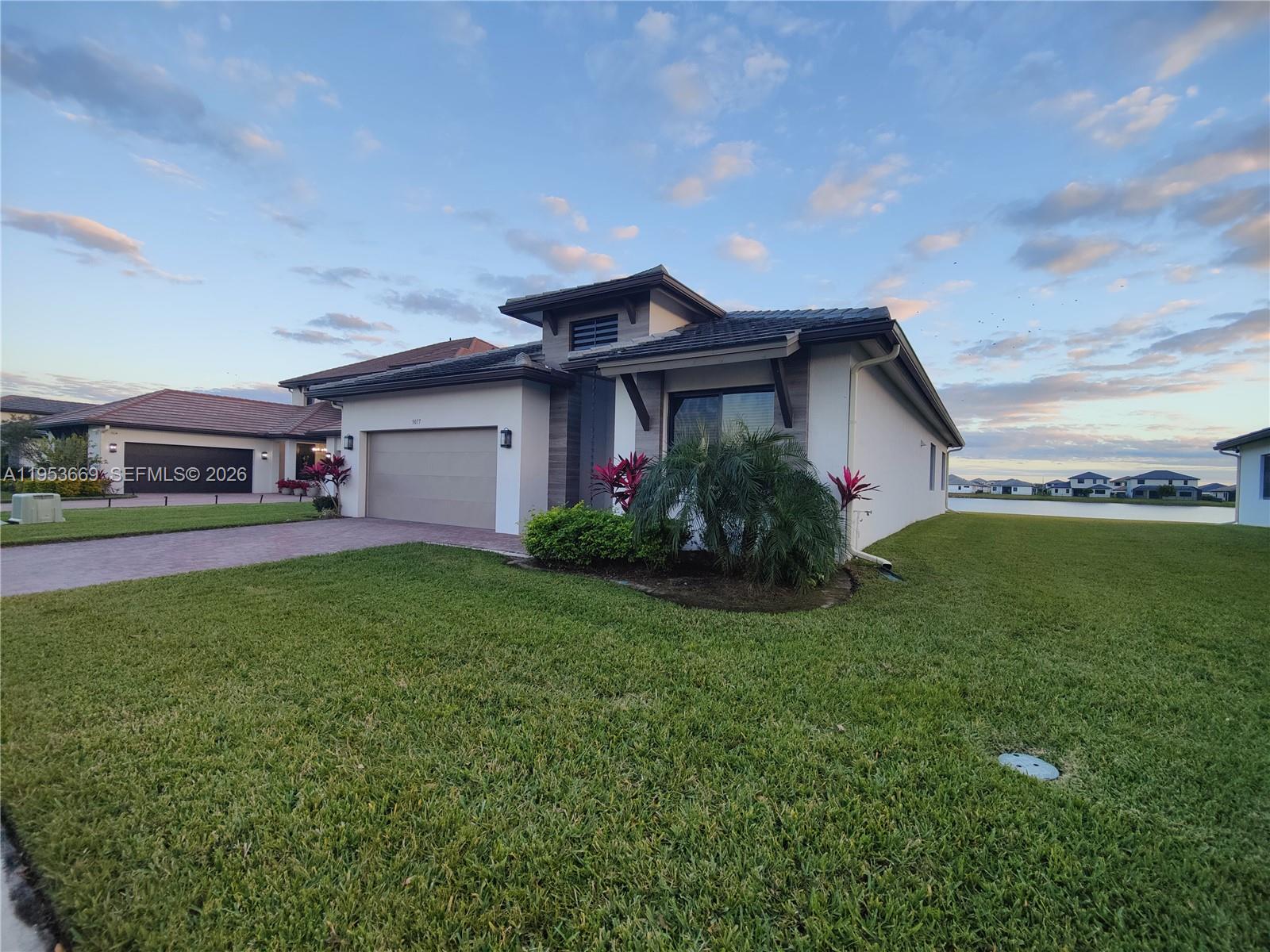 A single-story house with a garage and a landscaped front yard faces a lake — 5077 Gambero Way # 5077, Naples FL 34142, NAPLES, FL