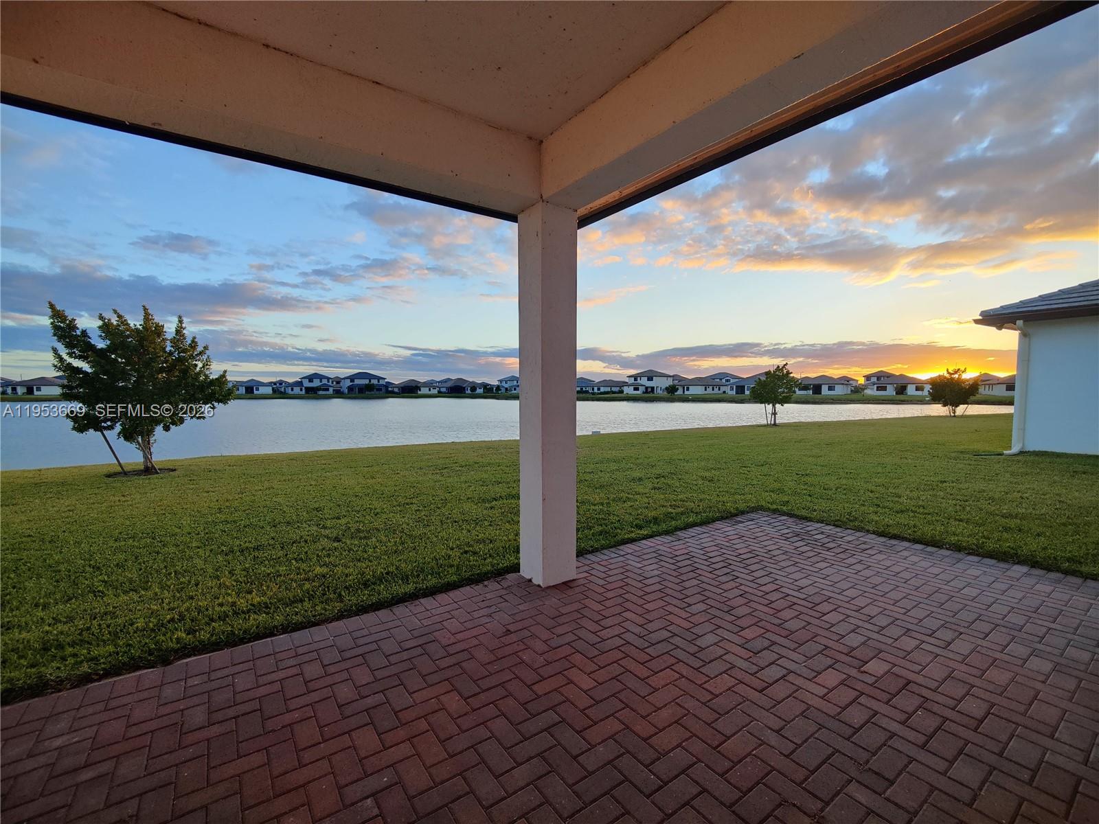 A paved patio overlooks a grassy lawn, a lake, and distant houses at sunset — 5077 Gambero Way # 5077, Naples FL 34142, NAPLES, FL