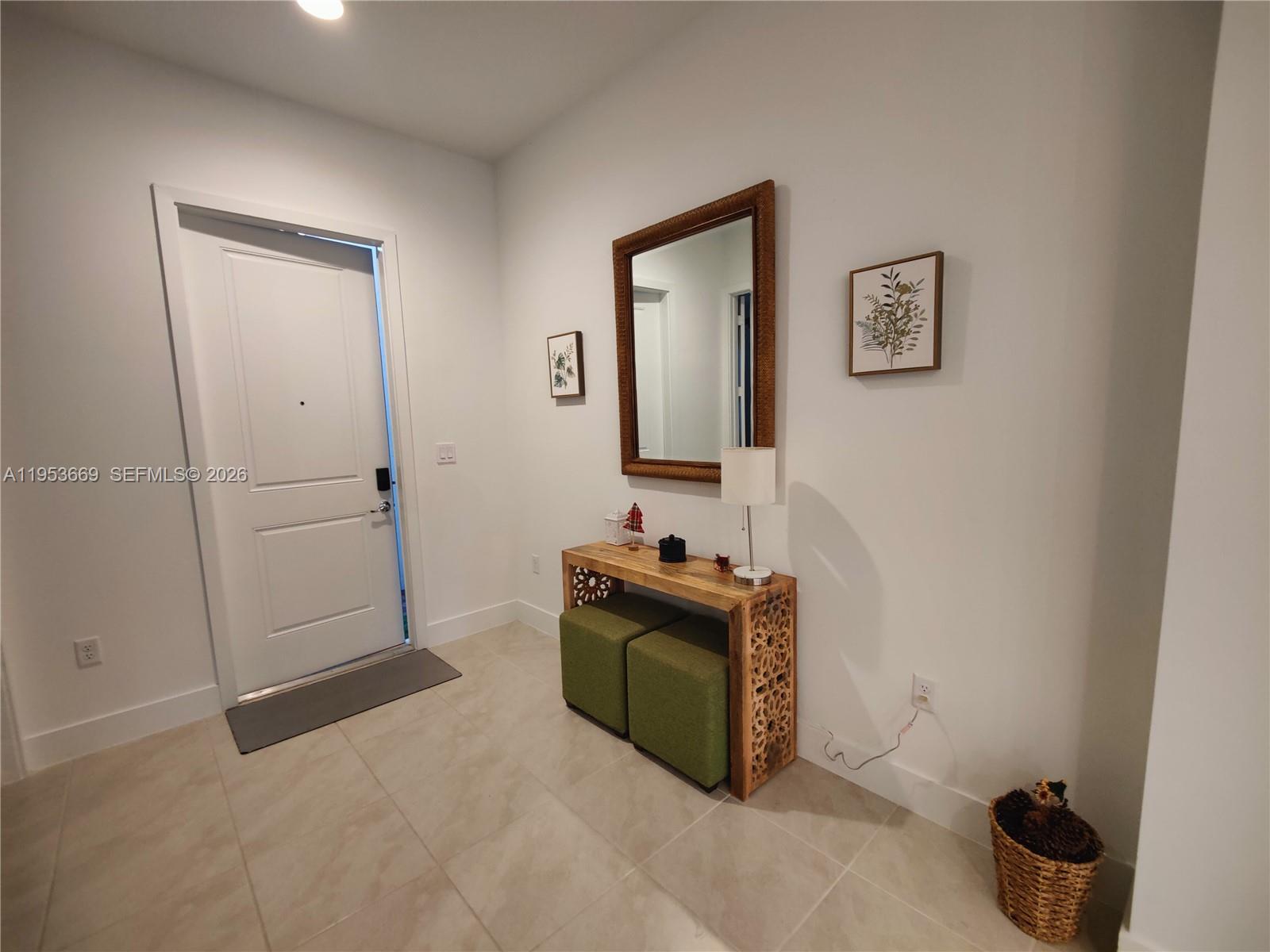 An entryway features a white door, a wooden console table with green ottomans, and a mirror — 5077 Gambero Way # 5077, Naples FL 34142, NAPLES, FL