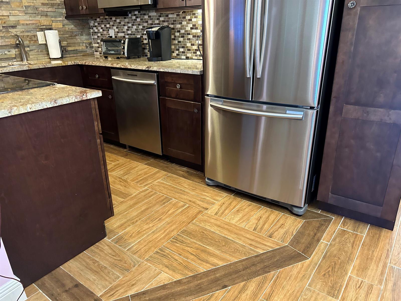 A kitchen features dark wood cabinets, stainless steel appliances, granite countertops, and patterned tile flooring — 3070 Cornwall D # D, Boca Raton FL 33434, BOCA RATON, FL