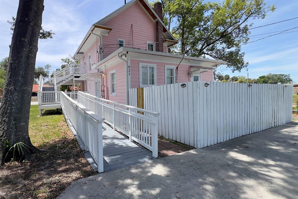 A pink two-story house features a white wooden wheelchair ramp and a white picket fence — 821 EMMETT STREET 2nd Floor, KISSIMMEE, FL