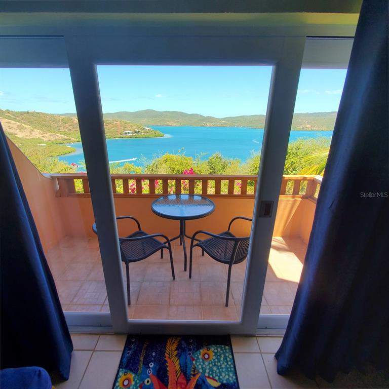 A balcony with a table and two chairs overlooks a bay and distant hills — C101 BAHIA MARINA CONDOMINIUM RESORT UNIT C101, CULEBRA, PR