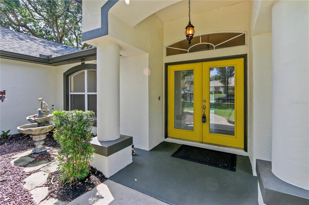 A covered entryway features a bright yellow double door, a stone fountain, and columns — 10814 VINEYARD COURT, CLERMONT, FL