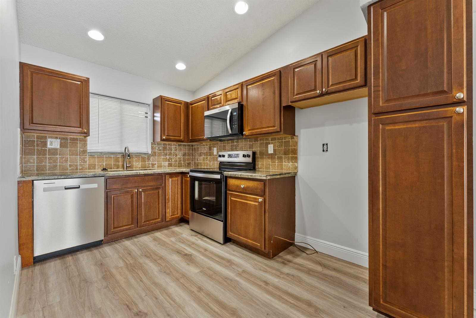 A kitchen features wood cabinets, stainless steel appliances, tile backsplash, and light wood-look flooring — 2900 Olivewood Terrace # 2010, Boca Raton FL 33431, BOCA RATON, FL