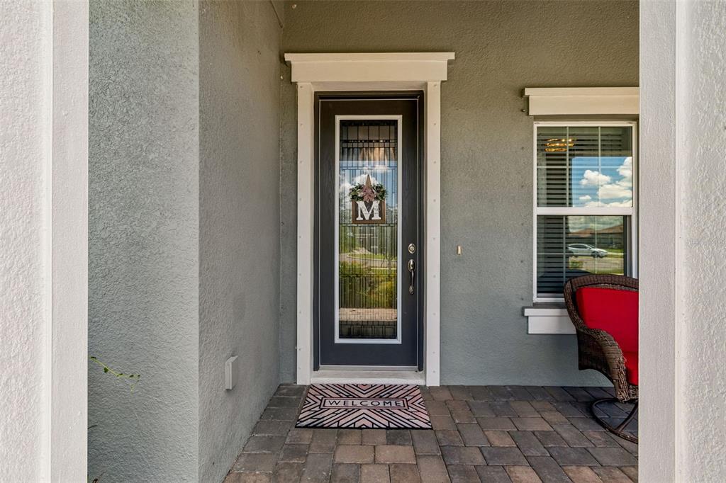 A covered porch with stone pavers, white columns, and two wicker chairs with red cushions — 10597 MEADOWRUN DRIVE, LITHIA, FL