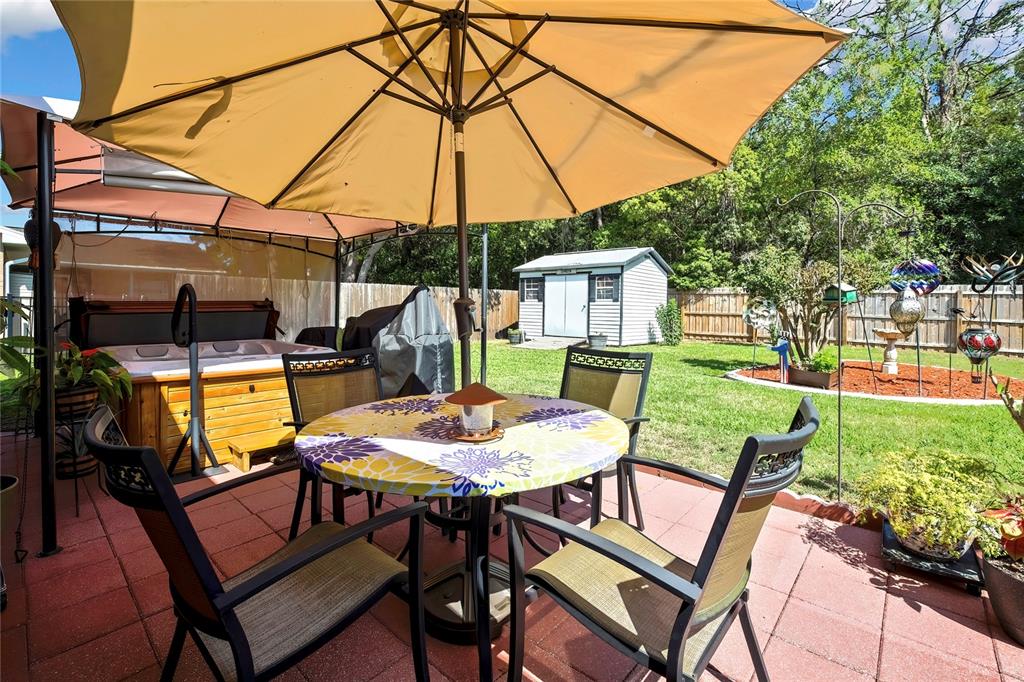 A patio features a dining set under a large umbrella, a hot tub, and a shed — 9045 GAYNOR STREET, SPRING HILL, FL