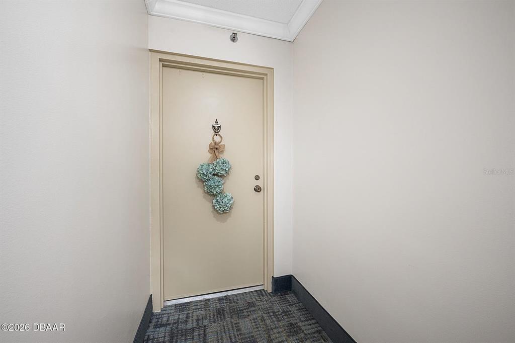 A beige door with a floral wreath is set in a small carpeted entryway — 1 OCEANS WEST BOULEVARD UNIT 6A6, DAYTONA BEACH, FL