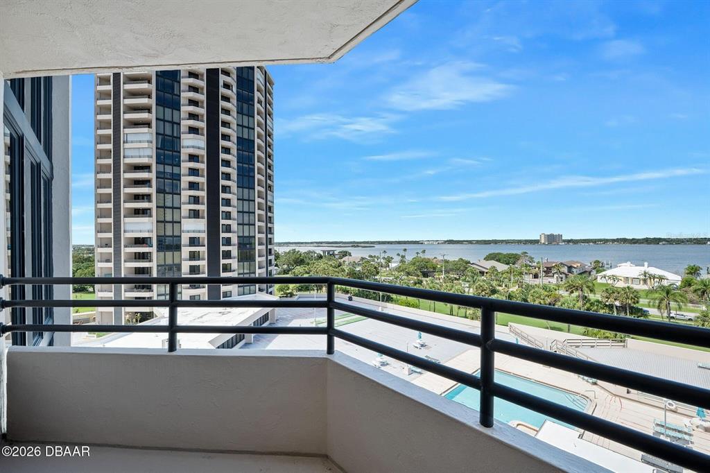 A balcony with a black metal railing overlooks a swimming pool, trees, and a river — 1 OCEANS WEST BOULEVARD UNIT 6A6, DAYTONA BEACH, FL