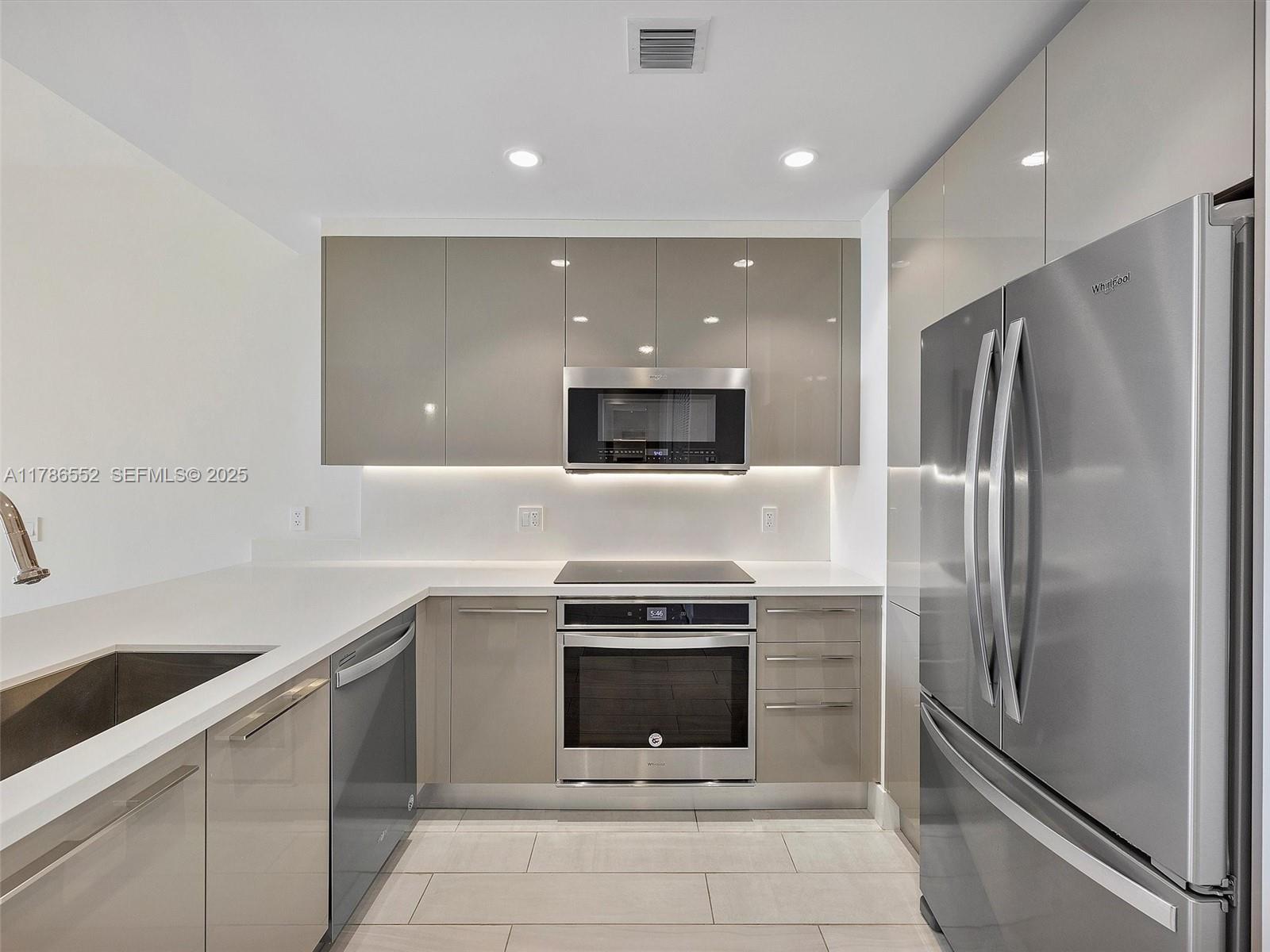 A modern kitchen features glossy taupe cabinets, stainless steel appliances, and white countertops — 2000 Metropica Way # 502, Sunrise FL 33323, SUNRISE, FL