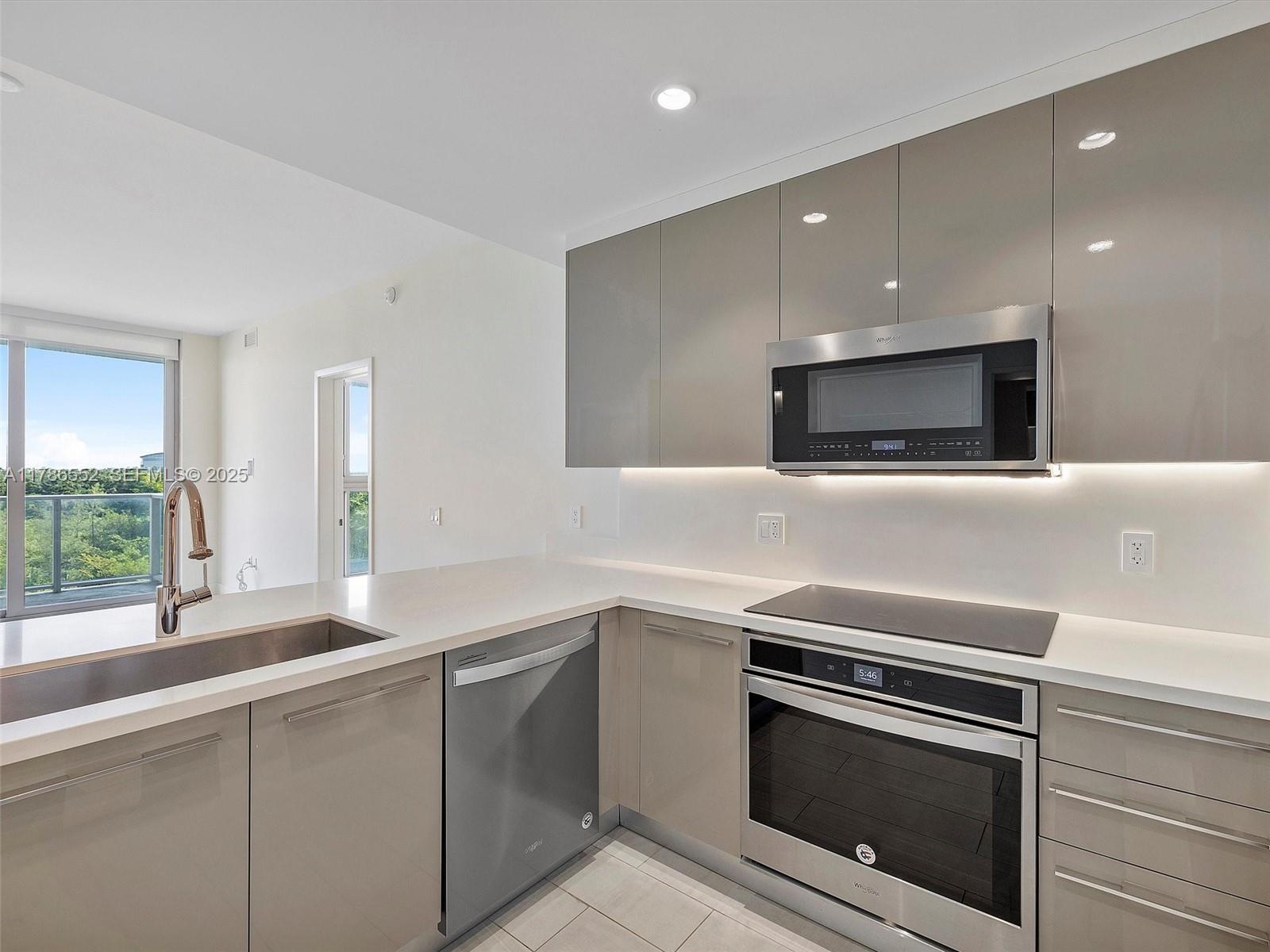 A modern kitchen features glossy taupe cabinets, stainless steel appliances, and white quartz countertops — 2000 Metropica Way # 502, Sunrise FL 33323, SUNRISE, FL