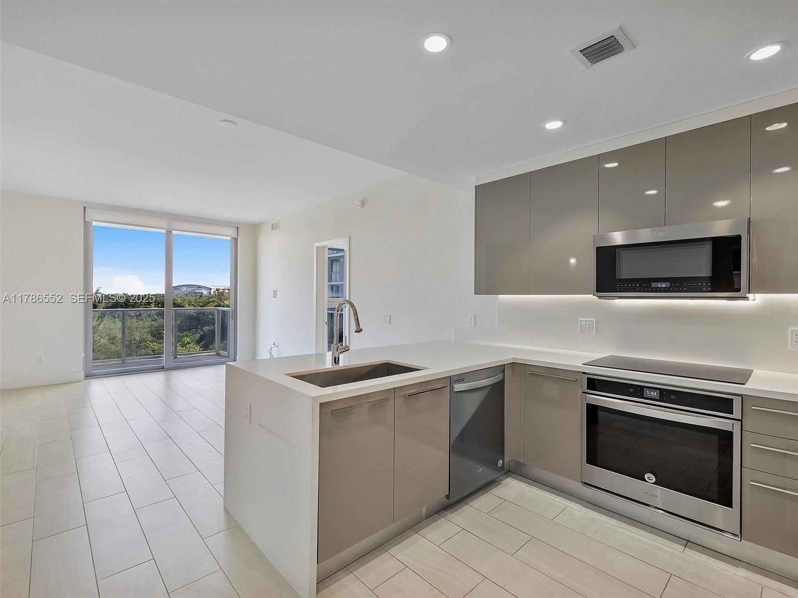 A modern kitchen features glossy gray cabinets, stainless steel appliances, and a white quartz island — 2000 Metropica Way # 502, Sunrise FL 33323, SUNRISE, FL