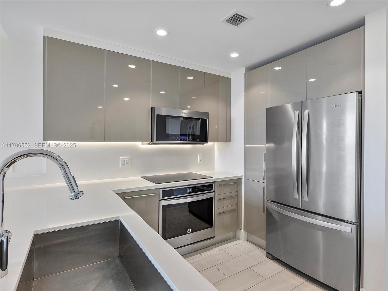 A modern kitchen features glossy taupe cabinets, stainless steel appliances, and white countertops — 2000 Metropica Way # 502, Sunrise FL 33323, SUNRISE, FL