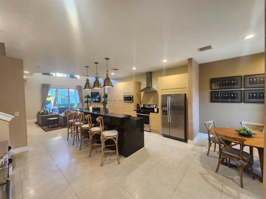 A modern kitchen features a black granite island, light wood cabinetry, and an adjacent dining area — 3160 PANTANAL LANE, KISSIMMEE, FL
