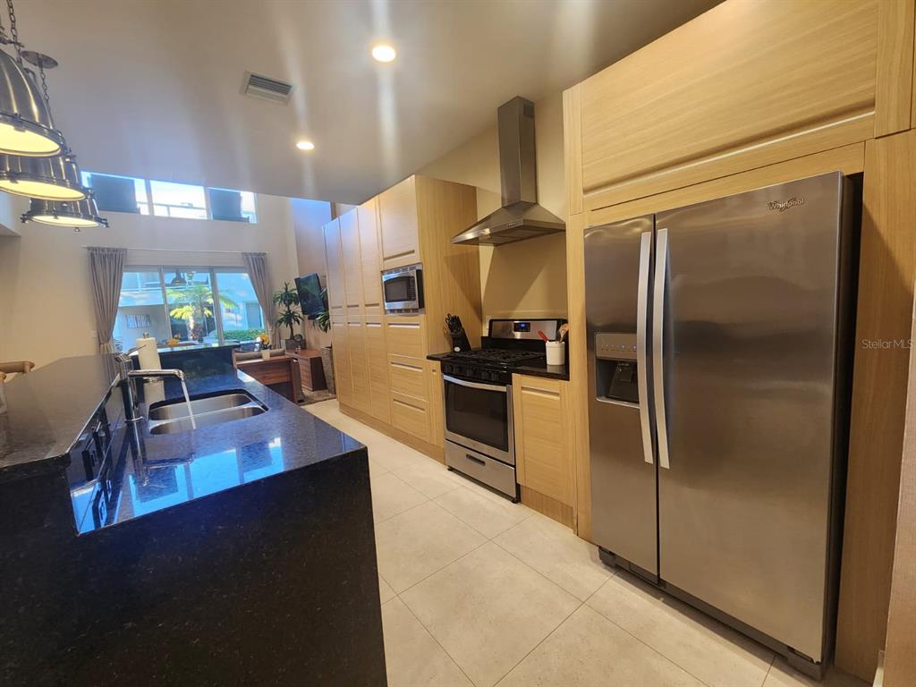 A modern kitchen features light wood cabinetry, stainless steel appliances, and a black granite island — 3160 PANTANAL LANE, KISSIMMEE, FL