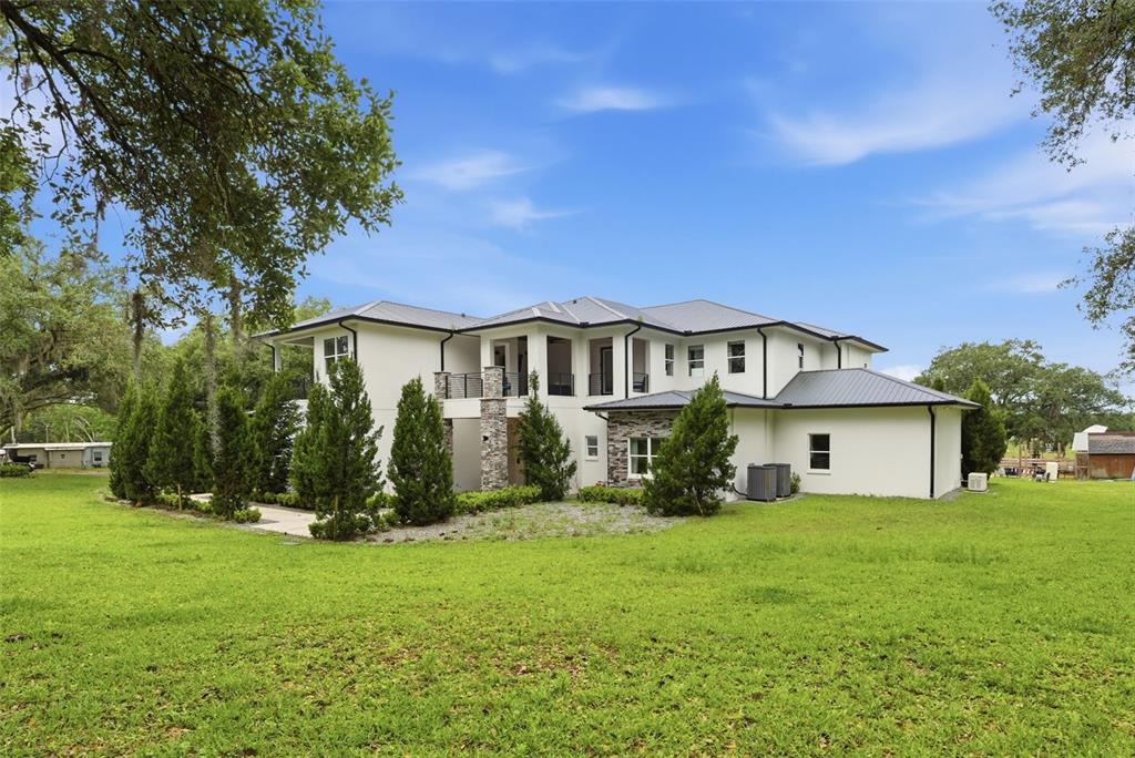 A two-story white house with a metal roof, stone accents, and surrounding green lawn — 8241 CASS ROAD, ZEPHYRHILLS, FL