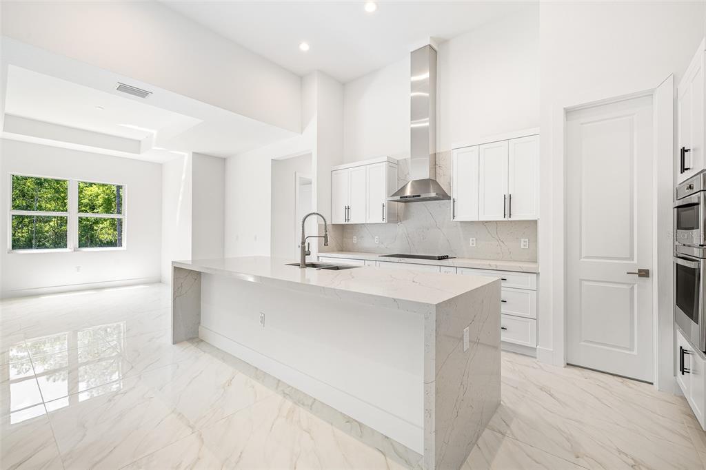 A modern white kitchen features a large marble island, stainless steel appliances, and tile flooring — 4531 YORKSHIRE LANE, KISSIMMEE, FL