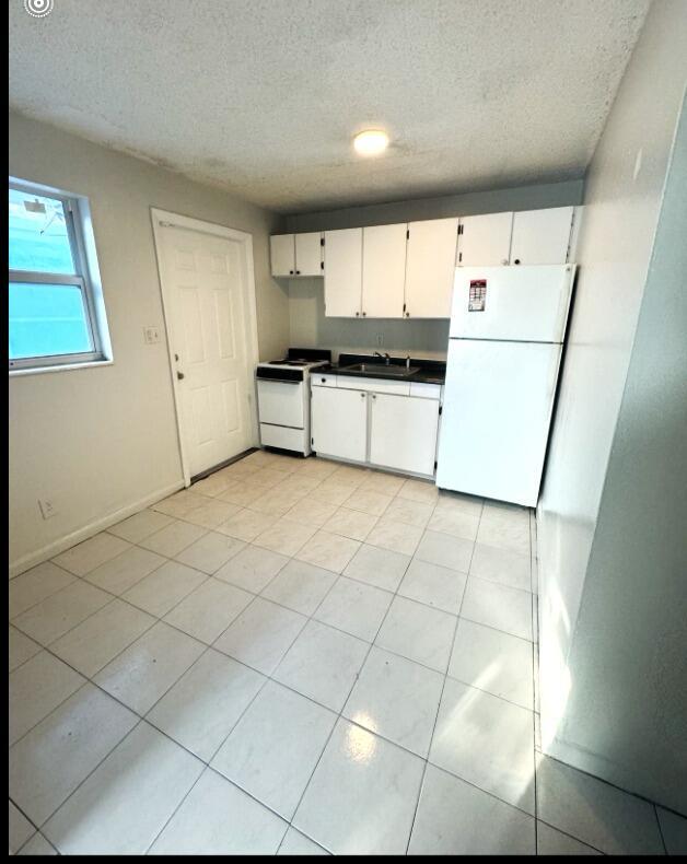 A small kitchen features white cabinets, white appliances, a tiled floor, and a side door — 720 NW 6th Avenue # 5, Pompano Beach FL 33060, POMPANO BEACH, FL